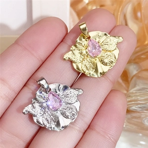 Macro shot of gold and silver flower pendants with pink teardrop stones on hand