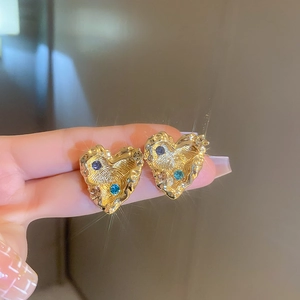 Detail of gold heart earrings with hammered texture and blue zircon inlay