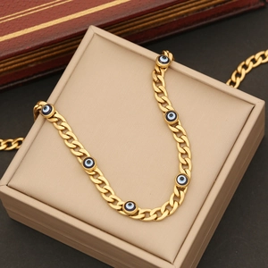 Golden Cuban chain necklace featuring blue evil eye charms on a beige display box