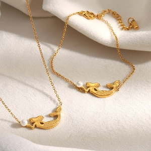 Détail de pendentifs sirène plaqués or 18K avec perles blanches sur tissu délicat