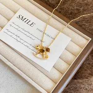 Close-up of golden rocking horse necklace with tiger eye stone on beige velvet tray