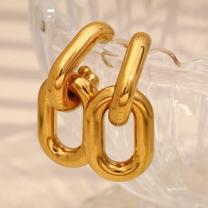 Detailed view of chunky hollow gold chain link earrings on transparent textured glass