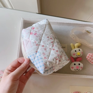 Détail d'une trousse à maquillage matelassée en coton fleuri et carreaux bleus