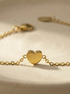 Macro shot of polished gold heart pendant with a fine O-chain minimalist bracelet