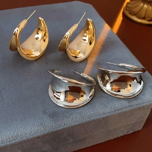 Close-up of polished C-shaped chunky hoop earrings in gold and silver on grey velvet