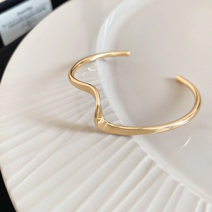 Macro shot of gold-plated wavy irregular open bangle on textured ceramic plate