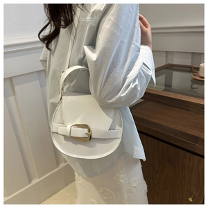 Detailed view of white leather crossbody bag with gold buckle on blue shirt model