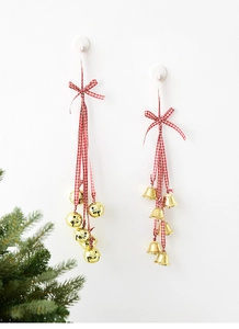 Detail of gold metal Christmas bells with red plaid ribbons hanging on a white wall