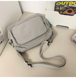 Flat lay of a grey nylon messenger bag with buckle strap on a minimalist desk setup