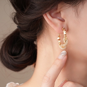Close-up of golden twisted rope hoop earrings with textured mesh finish on model
