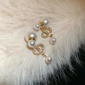 Gold plated zircon earring with CD logo and white pearls on soft velvet background