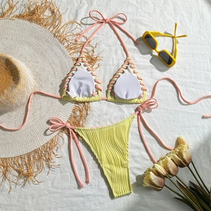 Close-up of ribbed yellow bikini with pink lace-up details on white linen background