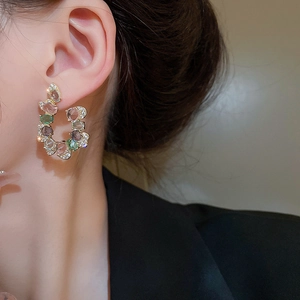 Detailed close-up of U-shaped gold earrings with colorful gemstones and small zircons