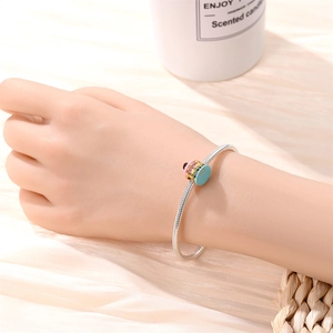 Macro shot of a silver snake chain bracelet featuring a colorful cake charm on a person's wrist