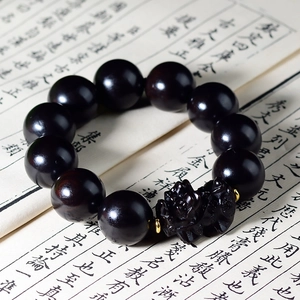 Dettaglio ravvicinato del bracciale di perline in legno scuro con ciondolo Pixiu nero