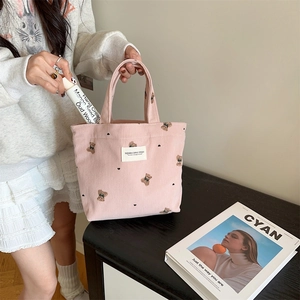 Pink corduroy handbag featuring cute bear embroidery held by a model in casual setting