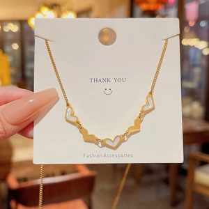 Close-up of golden necklace featuring white heart pendants displayed on a white gift card