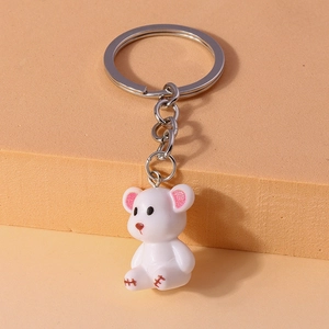 Close-up of a white resin bear keychain with pink ear accents on geometric prop