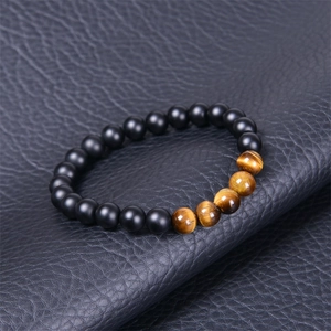 Détail des perles d'oeil de tigre et pierres noires mates sur surface grise texturée
