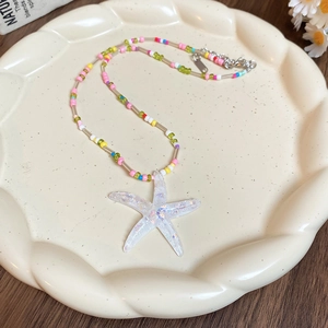 Colorful beaded necklace featuring a glitter starfish pendant on a ceramic wave plate