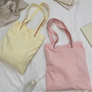 Détail de sacs cabas en toile avec bandoulières tissées à fleurs sur tissu blanc