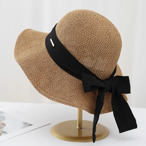 Dettaglio ravvicinato di un cappello di paglia marrone con fiocco nero e logo in metallo