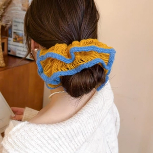 Detailed close-up of handmade yellow and blue knit flower hair tie on low bun