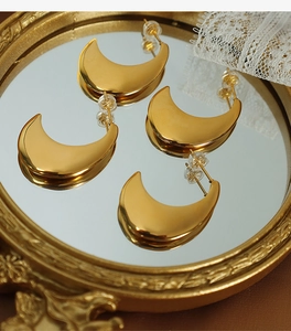 Detailed macro view of matte gold crescent earrings resting on a vintage mirror frame
