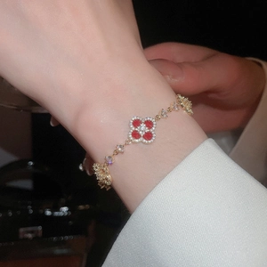 Close-up of 18k gold plated bracelet with red clover pendant and shimmering zircons on wrist