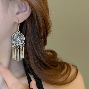 Close-up of vintage ethnic earrings with silver-tone pendants and fringe tassels on model