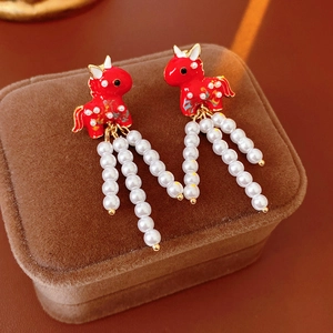 Detail of red enamel unicorn earrings with elegant pearl tassels on a jewelry box