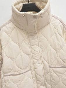 Detailed view of women's cream quilted jacket with stand collar and wave stitch pattern