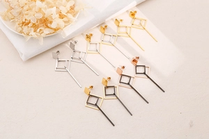 Detailed view of minimalist geometric drop earrings in multiple metallic finishes on texture