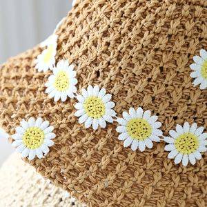 Detail of hand-woven straw hat featuring intricate white and yellow daisy crochet accents