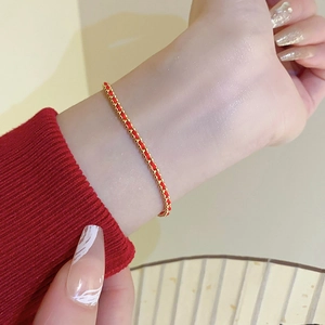 Close-up of a handmade red woven bracelet with gold-plated beads on a model's wrist