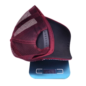 Detail view of burgundy mesh trucker hat with rhinestone brim on a scale for weight measurement