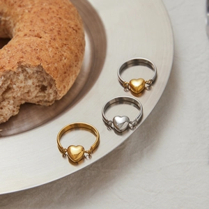 Minimalistische herzförmige Edelstahlringe in Gold und Silber auf einer Metallplatte