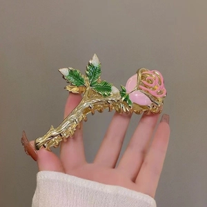 Detail of golden metal rose claw clip with pink oil-painted petals and green leaves