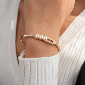 Close-up of golden open cuff bracelet with three pearls and inlaid rhinestones