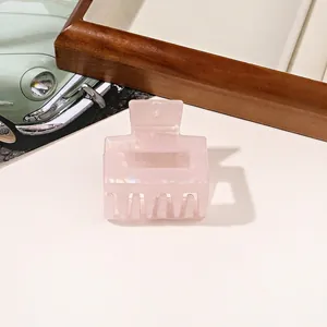 Pink mother-of-pearl textured hair claw clip with rectangle design on wooden tray