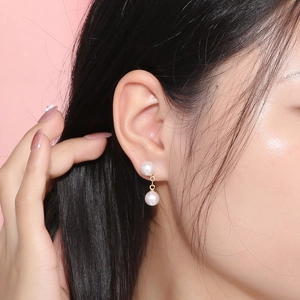 Détail de boucles d'oreilles dorées à double perle portées sur fond rose élégant