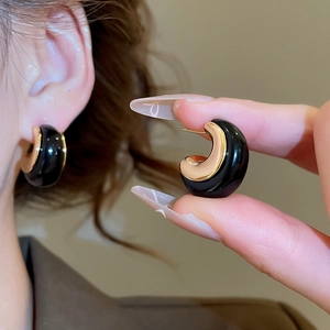 Close-up of 18k gold-plated and black resin C-shaped earrings on a model's ear