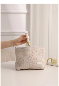 Detail of hand putting essence tube into beige woven cosmetic bag with zipper