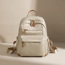 Detail view of beige nylon backpack featuring brown leather handles and dual front zipper pockets
