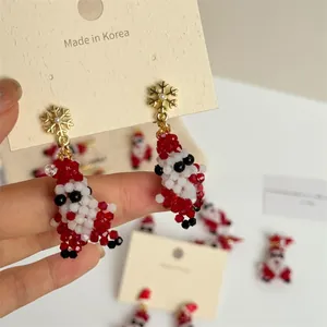 Close-up of handmade beaded Santa Claus earrings with a gold snowflake stud and pearl