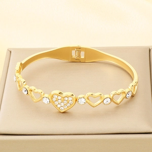 Close-up of golden hollow heart bracelet with white rhinestones on champagne velvet