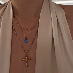 Detail of layered gold necklaces with a blue teardrop gemstone and beaded cross pendant