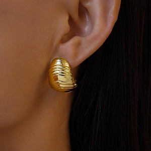 Gros plan d'une boucle d'oreille dorée texturée en forme de coquille sur un modèle