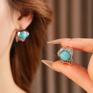 Close-up of vintage C-shaped silver earrings with round turquoise stones on ear