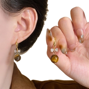 Gold bow earrings with tiger eye stone drop pendants shown on model and in hand